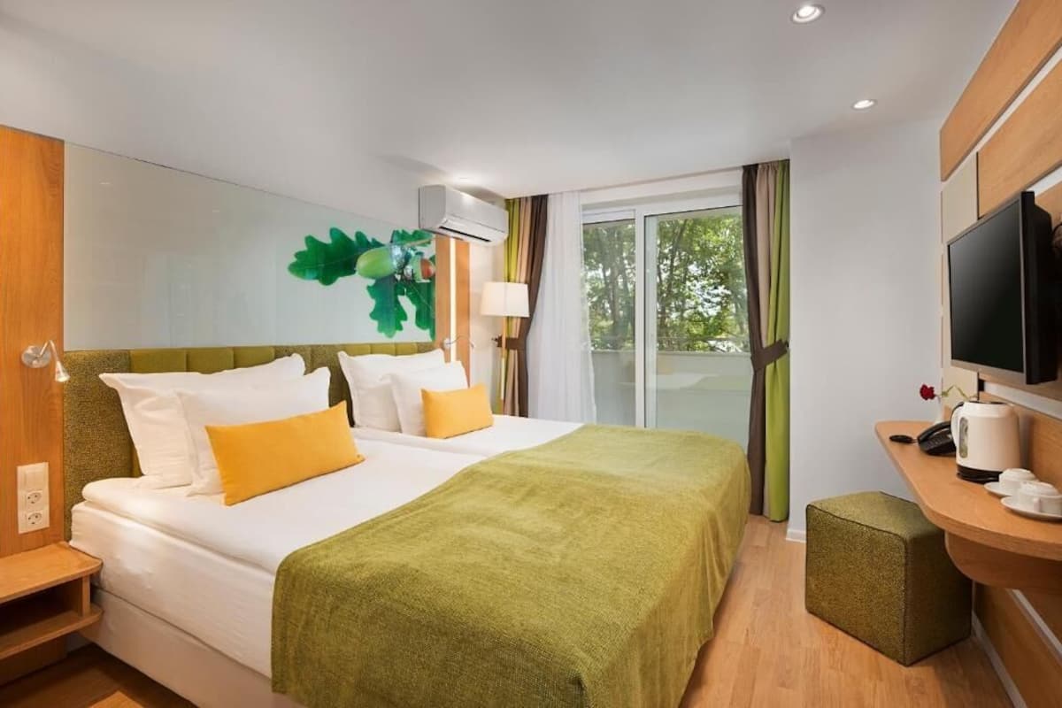 A hotel room with a bed, a desk with a TV, a coffee maker, and a window with curtains.