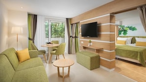 A modern hotel room with a green sofa, a round table, a TV mounted on the wall, and a bed with green bedding. - Forest Beach Hotel (Kiten)