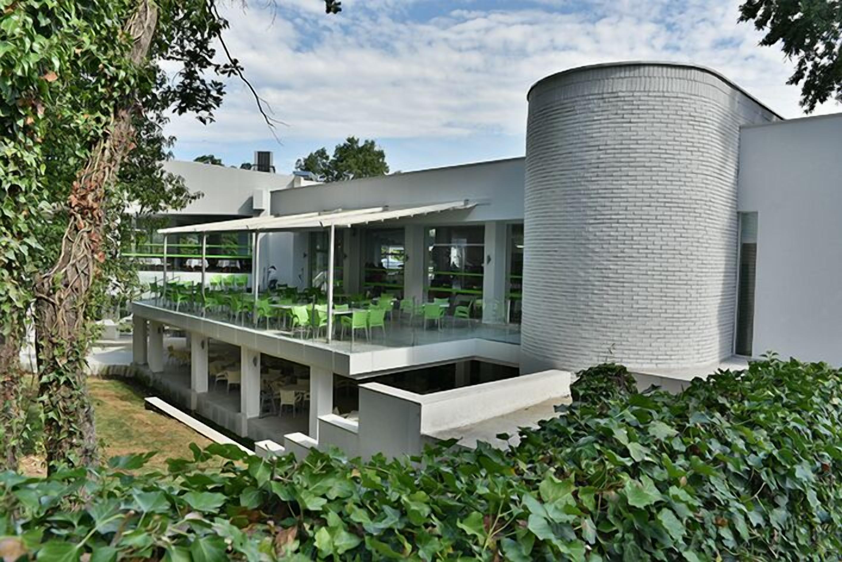 Een modern gebouw met een cilindervormige constructie, een overdekt buitenterrein en een tuin met klimop.