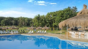 A swimming pool with lounge chairs and thatched umbrellas, surrounded by trees. - Forest Beach Hotel (Kiten)