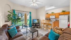 A compact living space with a sofa, coffee table, TV, kitchen area, and a sliding glass door to the outdoors. - Tranquil Townhouse 3 bed Lazy River Resort (Davenport)