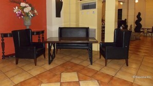 Een hal met een zwarte leren bank, twee zwarte fauteuils, een bloemenvaas en een betegelde vloer.