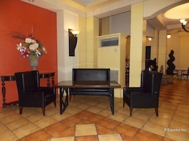 A lobby with a black leather sofa, two black armchairs, a vase of flowers, and a tiled floor.