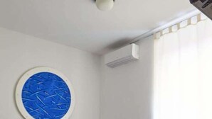 Ein Schlafzimmer mit einem Bett, einem blauen, runden Kunstwerk an der Wand, einem kleinen Nachttisch und einer Klimaanlage.