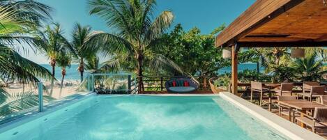 A pool area with a wooden deck, lounge chairs, and a view of the beach.