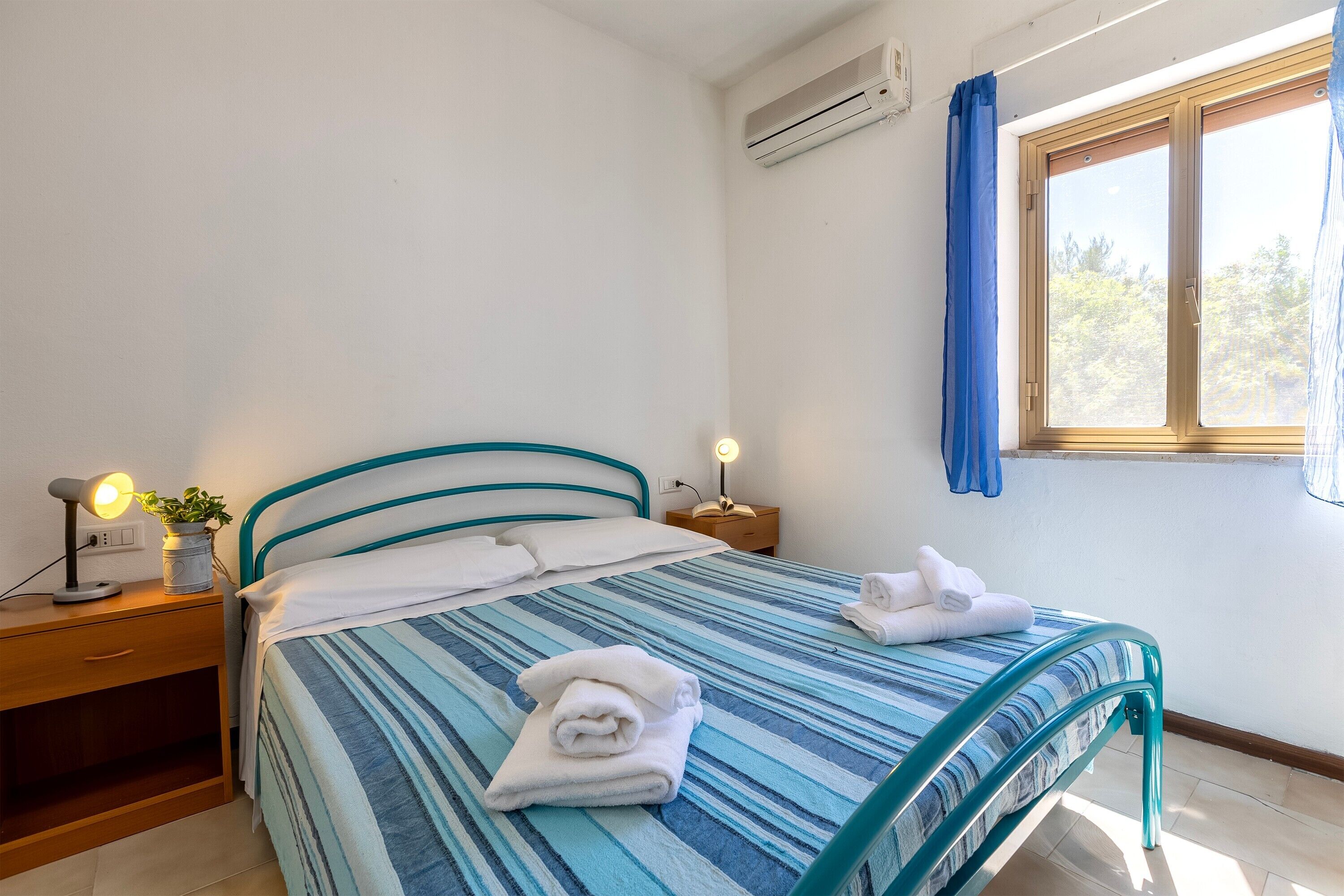 A bedroom with a bed, bedside table, lamp, and window.