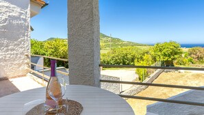 A round table with a bottle and glasses, a woven placemat, and a view of a vineyard and hills. - Apartment 'Con Terrazza' with Sea View, Wi-Fi and Air Conditioning (Valledoria)