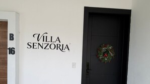Eine weiße Wand mit dem Schild "Villa Senzoria" und einer schwarzen Tür mit einem Kranz.