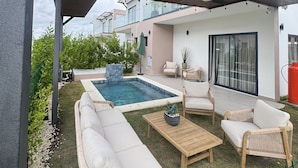 A modern outdoor living area with a pool, lounge chairs, and a covered patio. - NOK Modern 3BR Villa With Patio by Vistacana (Punta Cana)