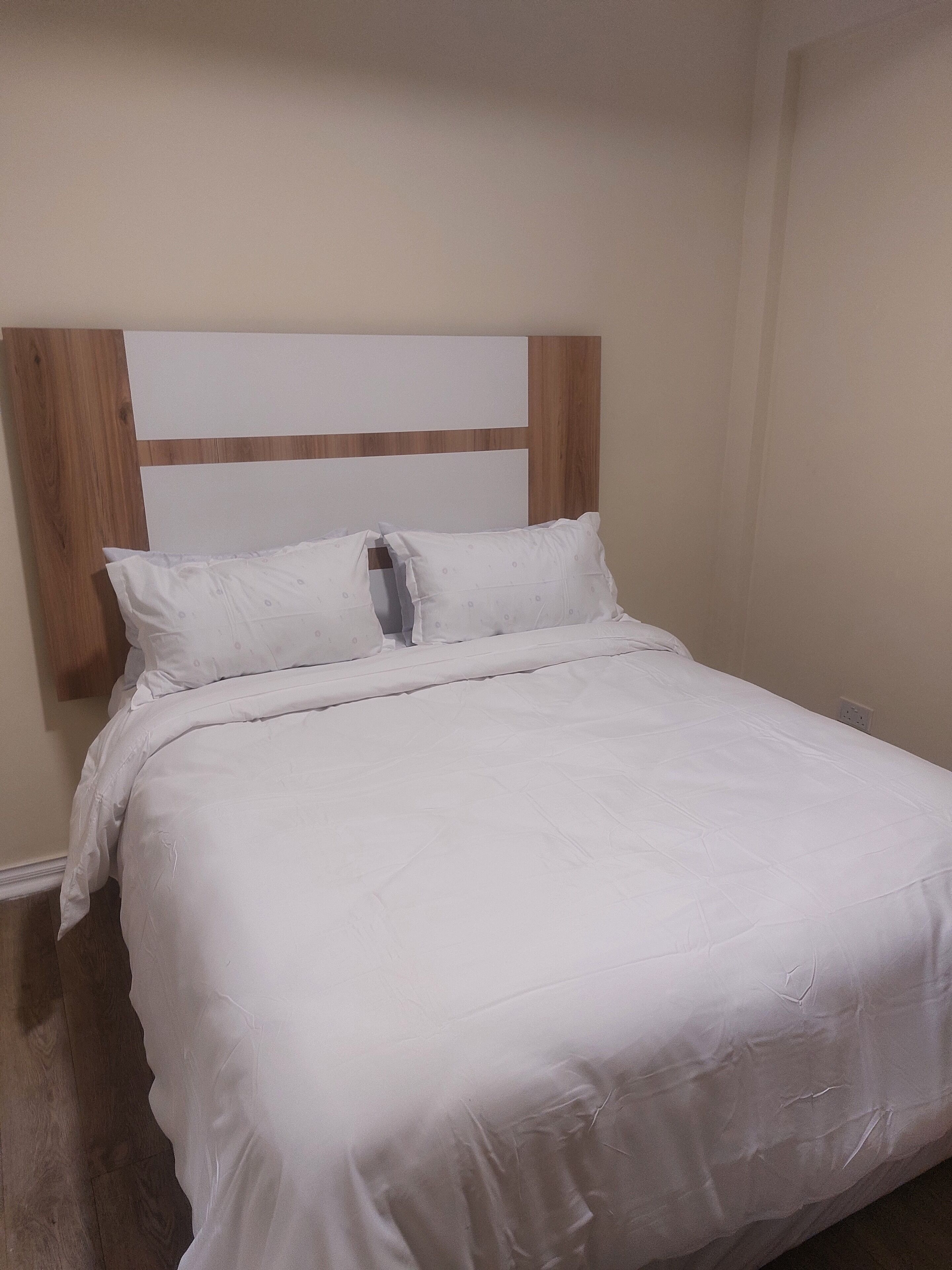 Een net opgemaakt bed met witte beddengoed en een houten hoofdbord.