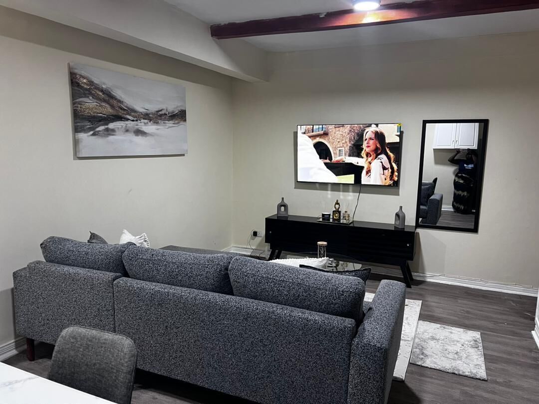 Una sala de estar moderna con un sofá gris, un televisor de pantalla plana montado en la pared, un mueble de entretenimiento negro y un cuadro sobre el sofá.