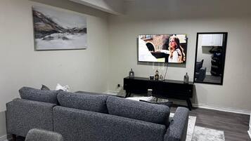 Una sala de estar moderna con un sofá gris, un televisor de pantalla plana montado en la pared, un mueble de entretenimiento negro y un cuadro sobre el sofá.