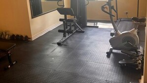 A gym with exercise equipment, a bench, and a window with a view of parked cars. - 24blouieville (Lusaka)