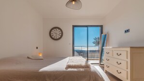 Ein Schlafzimmer mit einem Bett, einem Schminktisch, einer Uhr und Blick ins Freie.