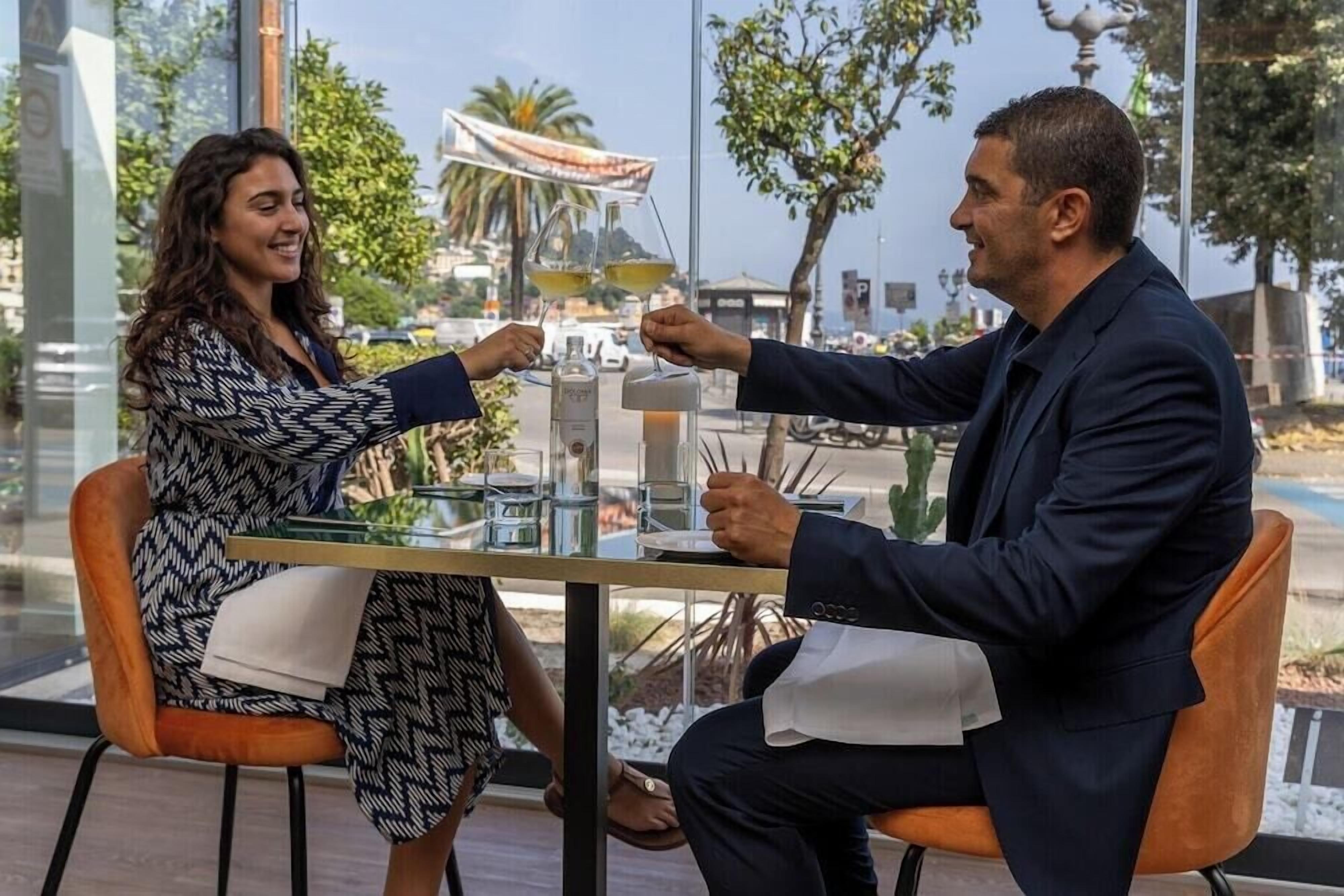 Dos personas sentadas en una mesa con una copa de vino, una botella y un vaso de agua.