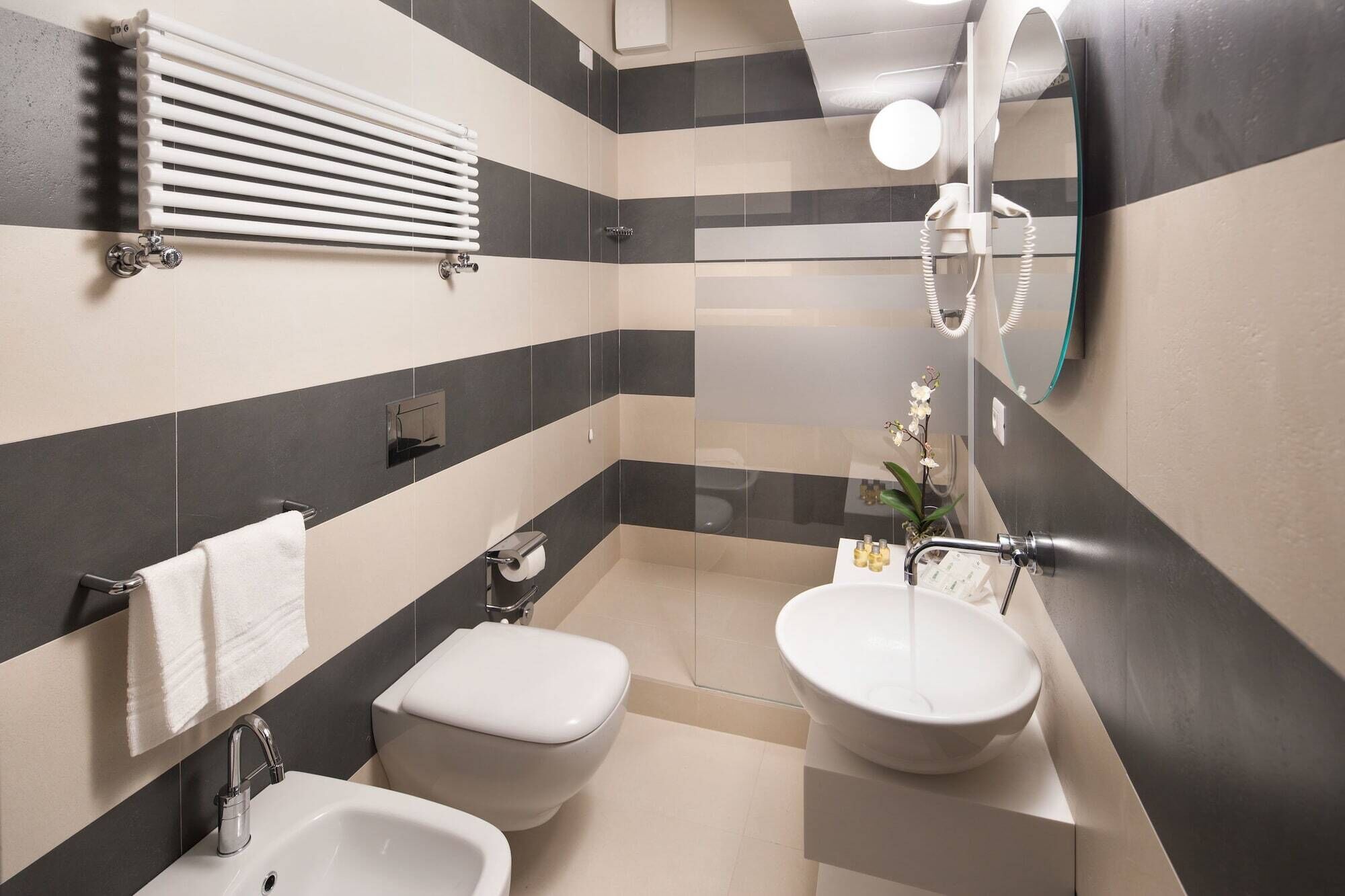 Et moderne badeværelse med bidét, toilet, vask og spejl.