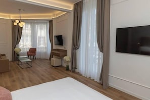 Moderni hotellihuone, jossa on suuri sänky, työpöytä, tuoli, televisio ja sohva.