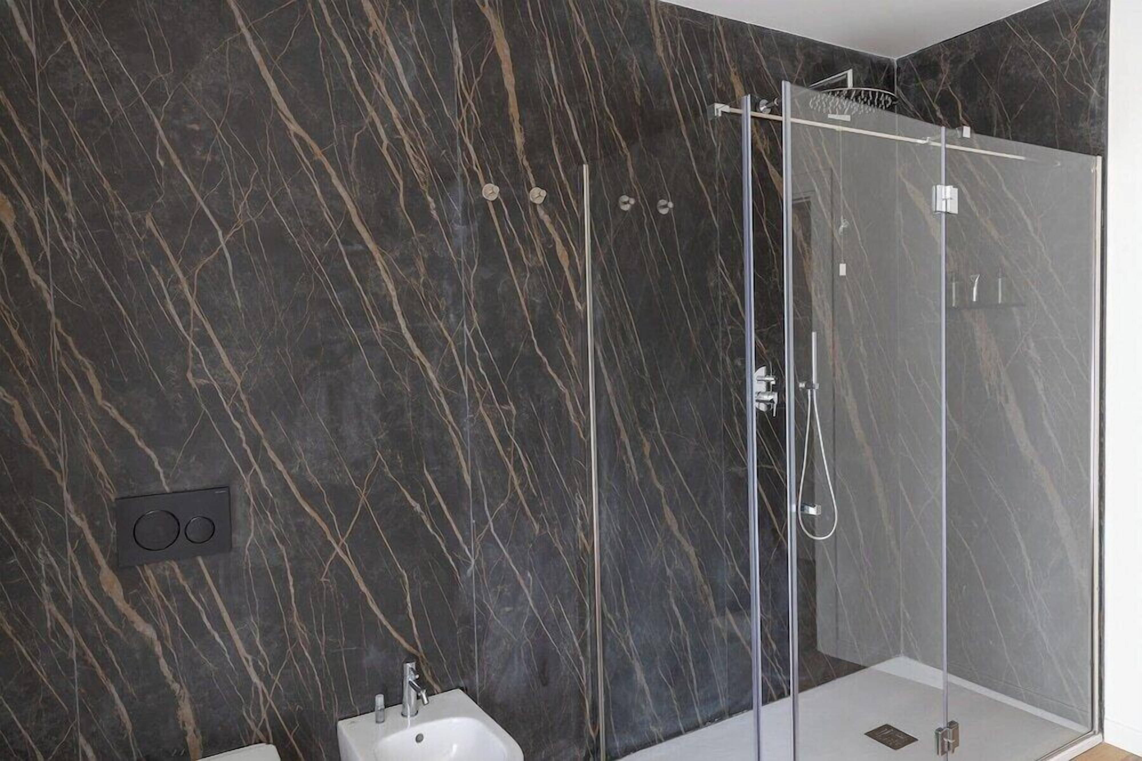 Ein modernes Badezimmer mit einer Duschkabine aus Glas, einem Bidet und einer Marmorwand.