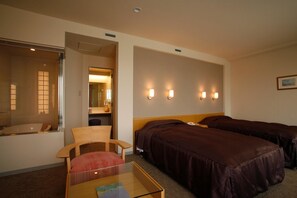 A hotel room with two beds, a chair, a small table, and a bathroom with a mirror and sink. - Furano Hotel (Furano)