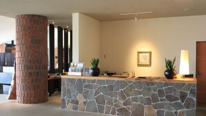 A reception area with a stone counter, a large brick pillar, and a framed picture on the wall. - Furano Hotel (Furano)