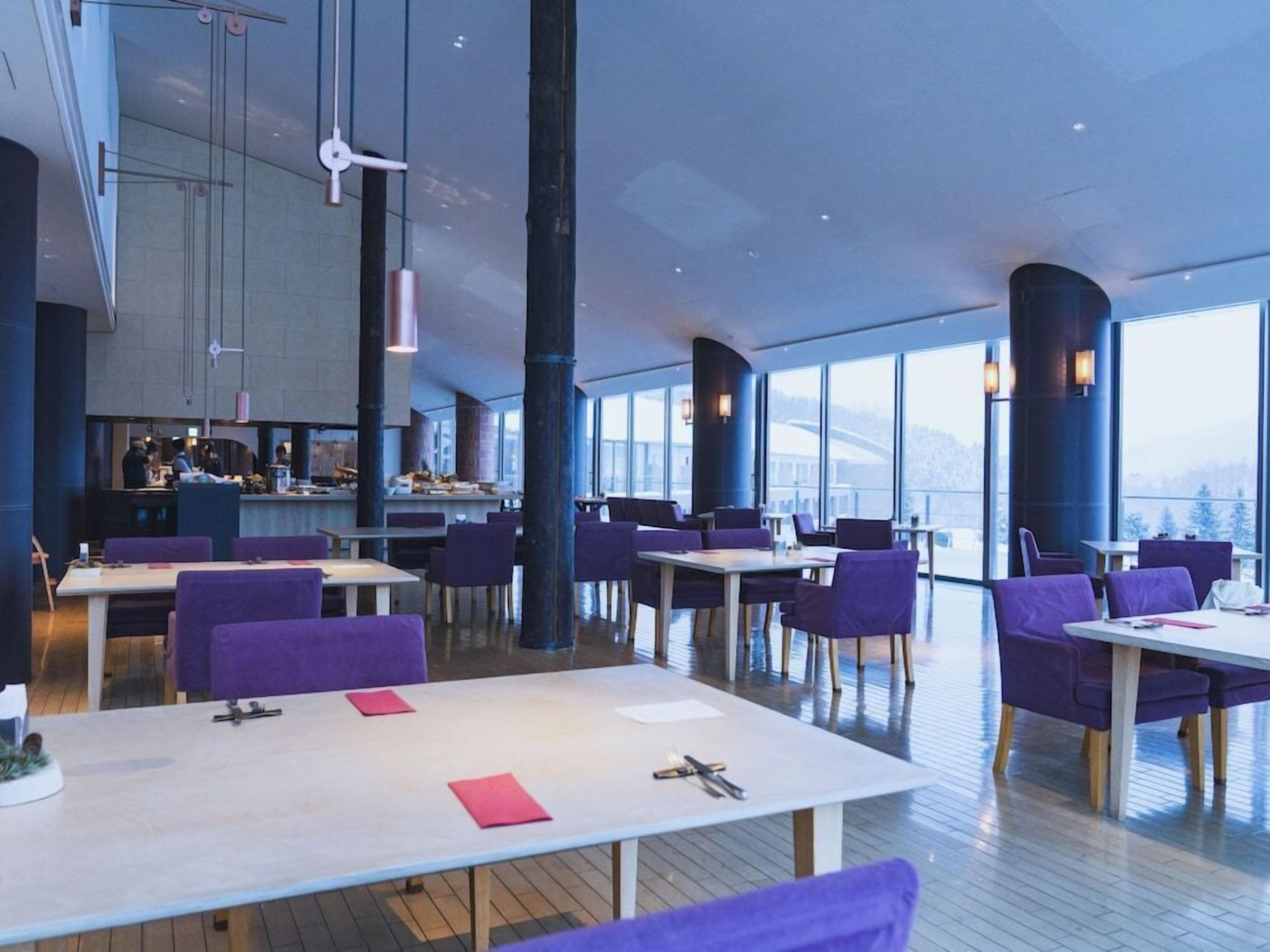 A modern restaurant with high ceilings, large windows, and purple seating.