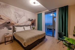Un dormitorio moderno con una cama grande, vista al mar por la ventana y un mural en la pared.