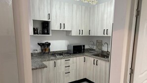 Una cocina moderna con alacenas de madera clara, encimeras de granito, microondas y estufa a gas.