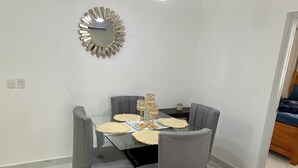 Un comedor con mesa de vidrio, sillas tapizadas en gris y un espejo decorativo en la pared.
