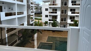 Edificio residencial de varios pisos con balcones, piscina y vista a una zona arenosa con palmeras.