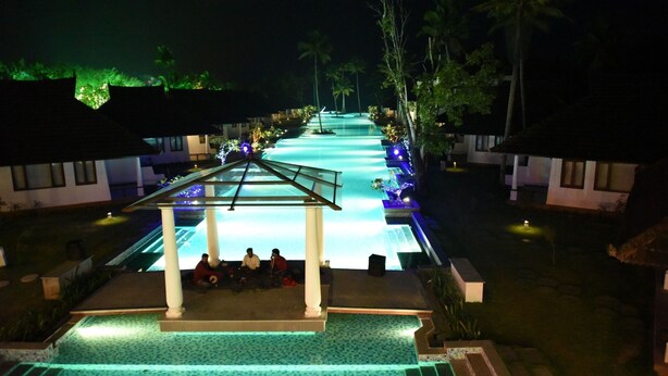A pool area with a covered seating area and palm trees. - Aveda Kumarakom (Kottayam)