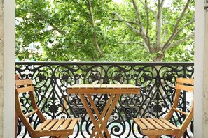 A wooden table and two chairs on a balcony with ornate black metal railings and a view of green trees. - Lovely Apartment Center of Paris (Paris)