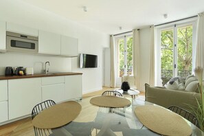 A modern kitchen with a flat-screen TV, a dining area with a glass table and chairs, and a sofa with a view of the outdoors. - Lovely Apartment Center of Paris (Paris)
