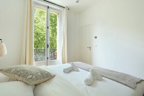 A hotel room with a large window, a bed with white linens, and a view of greenery outside. - Lovely Apartment Center of Paris (Paris)
