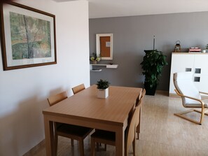 Un coin repas avec une table et des chaises en bois, une plante en pot, un meuble blanc et un tableau encadré accroché au mur.