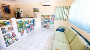 Un espace d’accueil comprenant un canapé, un panneau d’affichage avec des brochures de voyage, un comptoir et une fenêtre avec des stores.