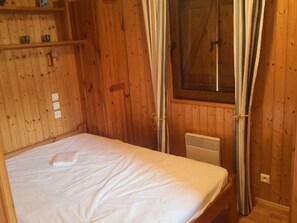 Ein Zimmer mit Holzboden, einem Bett, einem Fenster mit Vorhängen und einer Heizung.