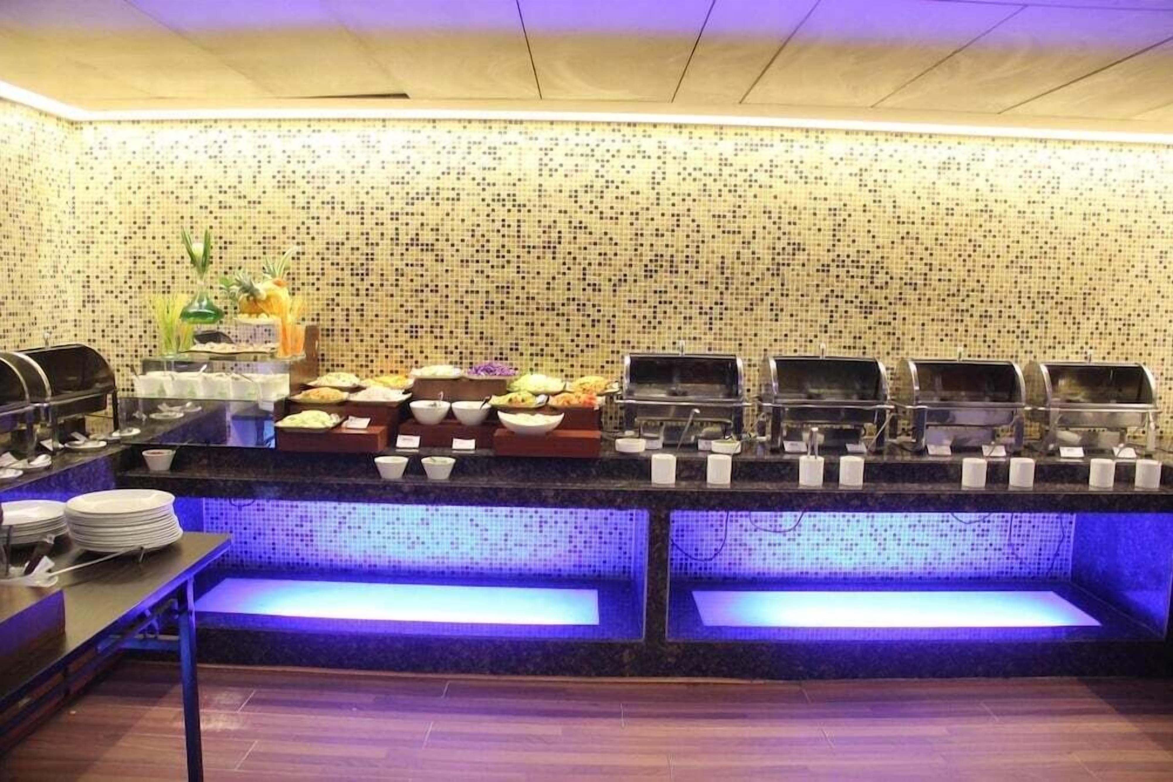 A buffet setup with various food items and a tiled wall in the background.