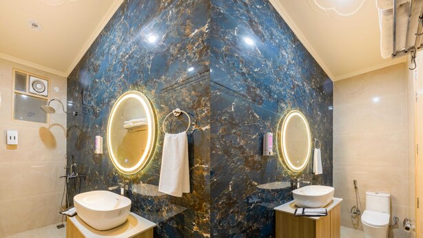 A modern bathroom with two sinks, marble walls, and a large mirror with illuminated edges. - Hotel Silver Star (Greater Noida)