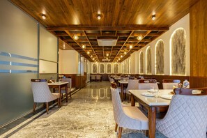 A spacious dining area with wooden ceiling beams, multiple tables, and chairs. - Hotel Silver Star (Greater Noida)