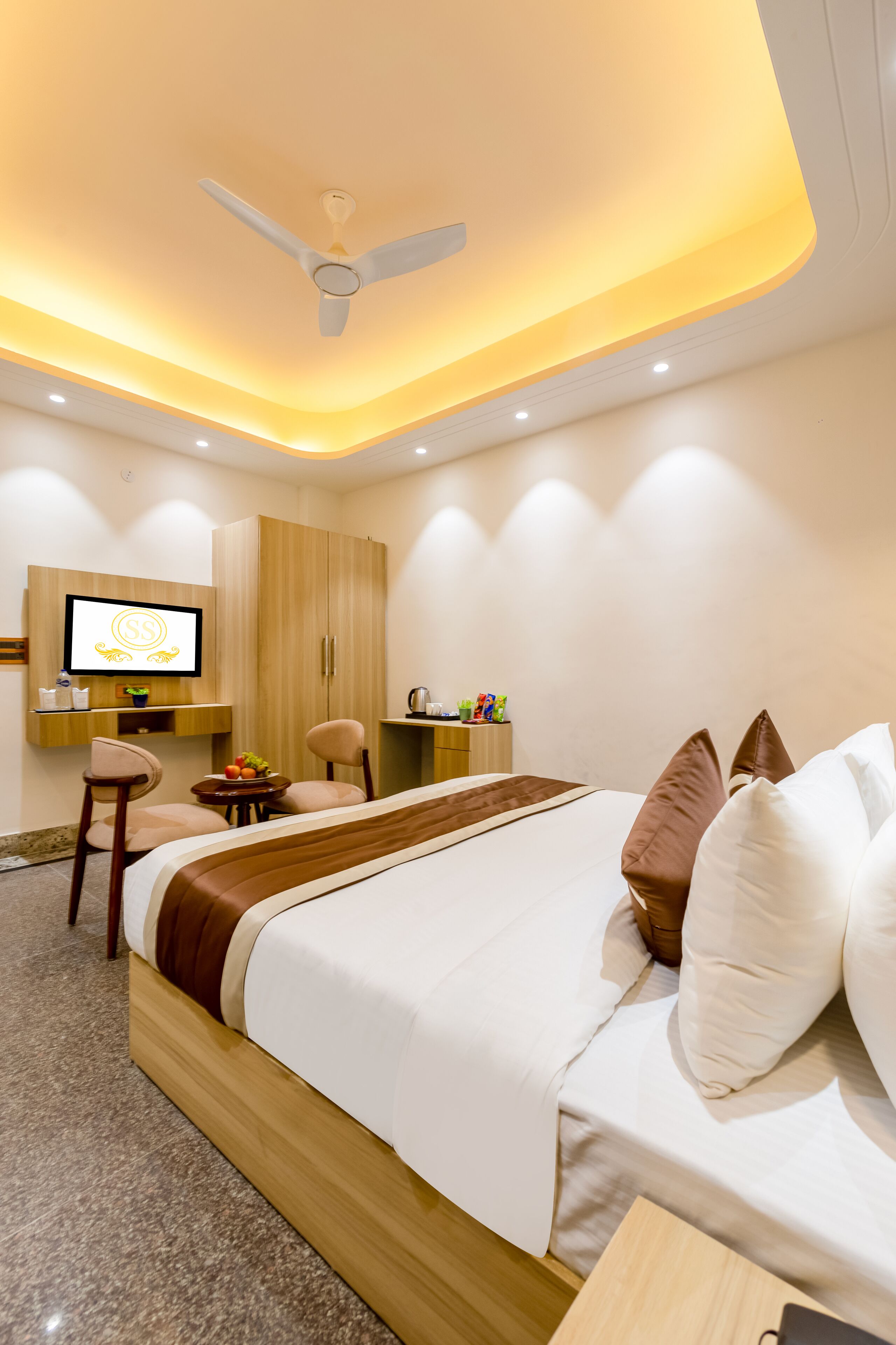 Een moderne hotelkamer met een groot bed, een bureau met stoel, een televisie en een plafondventilator.