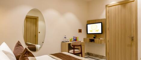 A hotel room with a bed, a ceiling fan, a TV, a mirror, and a wooden door.
