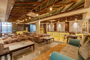 Un vestíbulo espacioso con techo alto, vigas de madera y suelo de mármol. Hay varias zonas de estar con sofás y una zona de bar con mostrador de mármol.