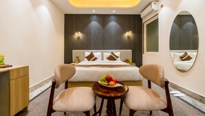 A hotel room with a bed, two chairs, a small table with fruit, and a mirror on the wall. - Hotel Silver Star (Greater Noida)