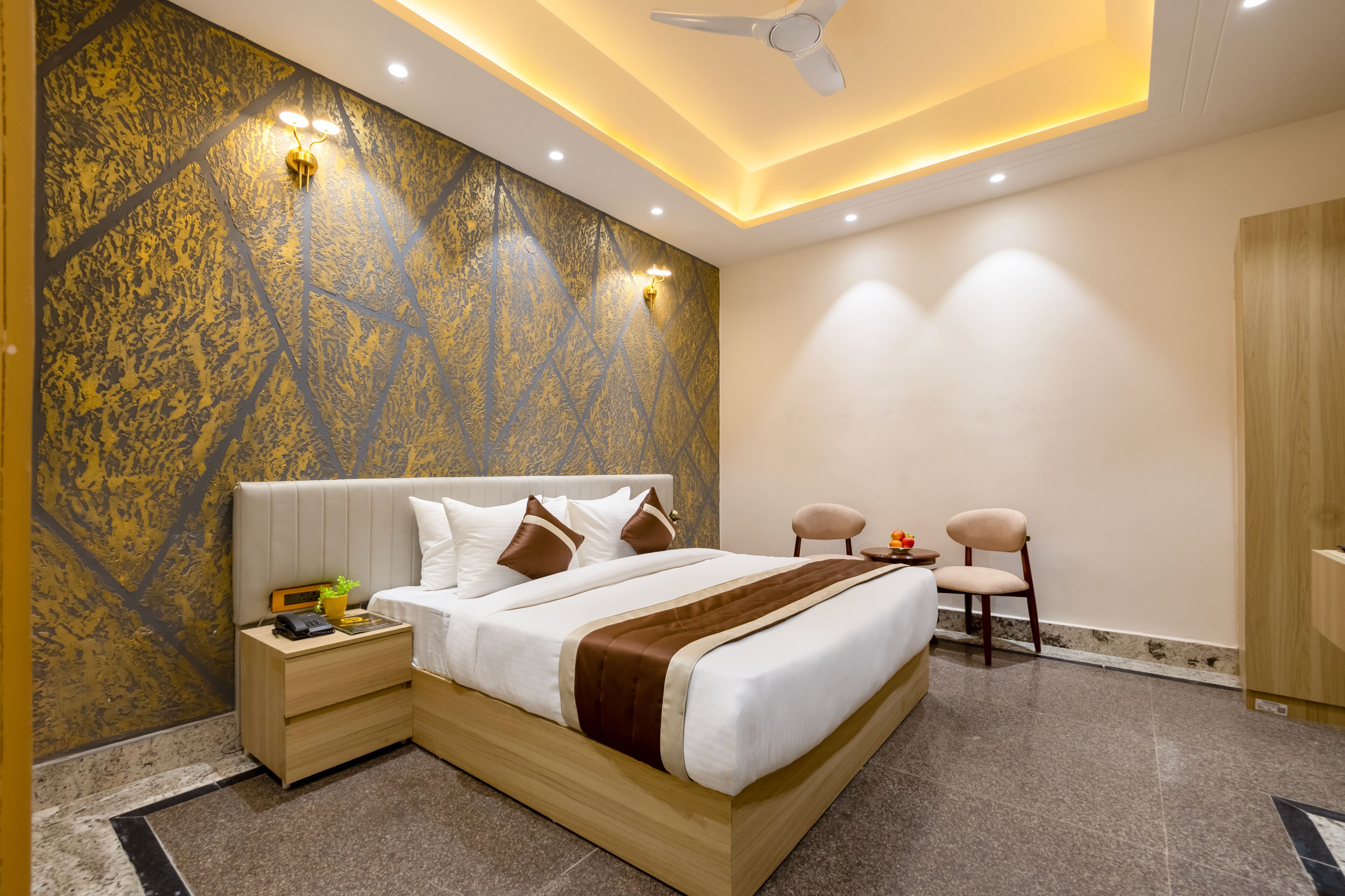 A modern hotel room with a large bed, bedside tables, a nightstand, a ceiling fan, and a wall-mounted light fixture.
