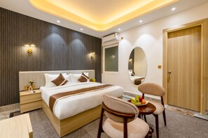 A modern hotel room with a large bed, bedside tables, a mirror, and a dining area with chairs. - Hotel Silver Star (Greater Noida)