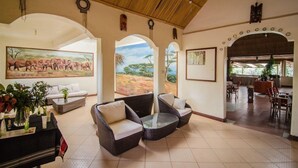 A spacious lobby with a high ceiling, a large painting of elephants, and a view of the outdoors through an archway. - Sentrim Mara Lodge (Maasai Mara)