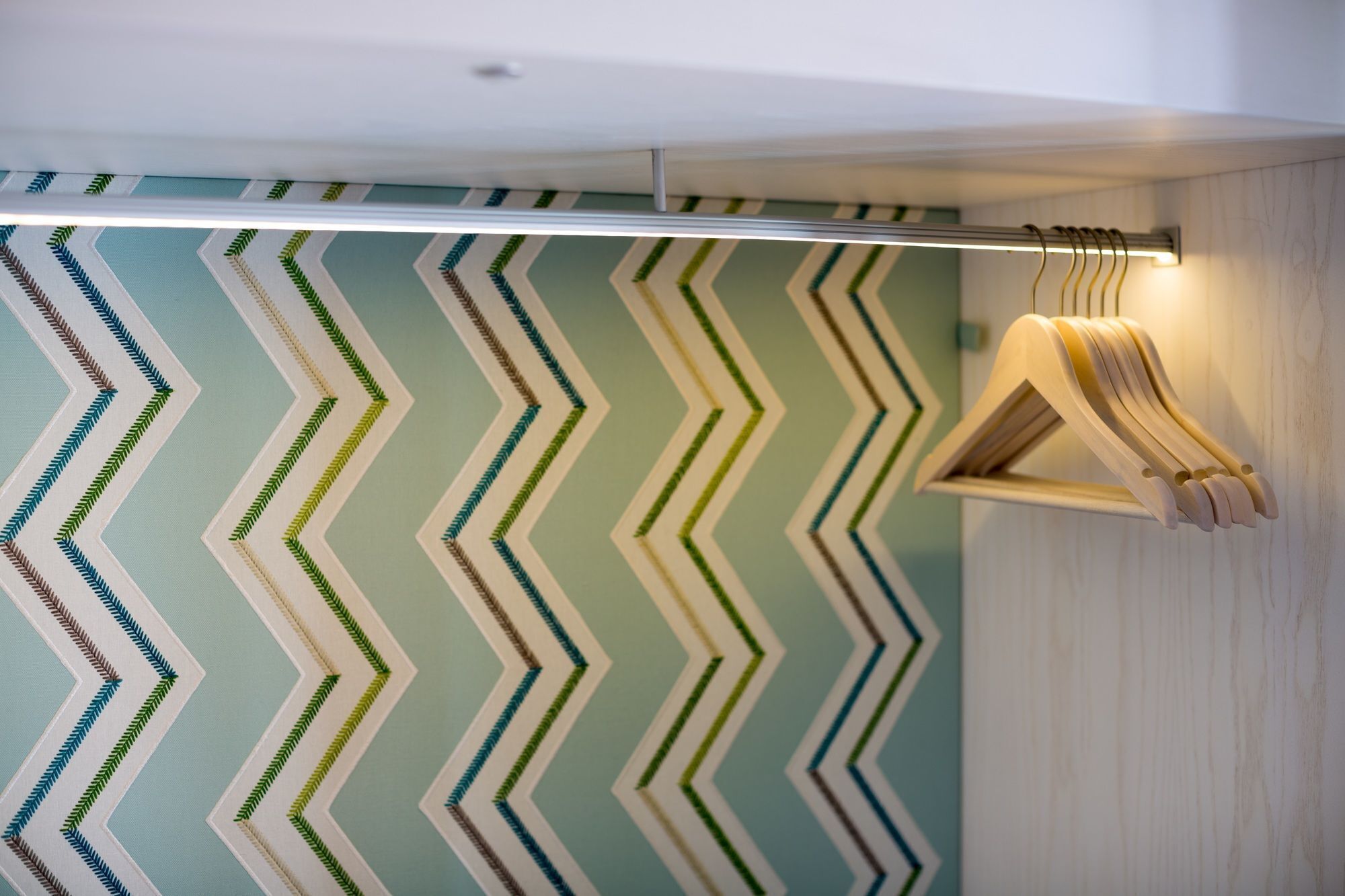 A room with a chevron-patterned wall and a wooden coat rack with a light fixture above it.