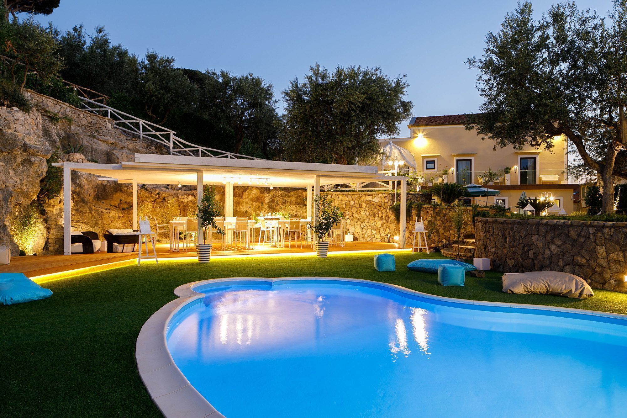A swimming pool with a covered outdoor seating area, stone walls, and a stone staircase.
