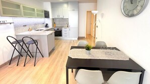 Una cocina moderna con comedor, que incluye un reloj de pared grande, una pequeña isla con taburetes de bar y una mesa de comedor con sillas.