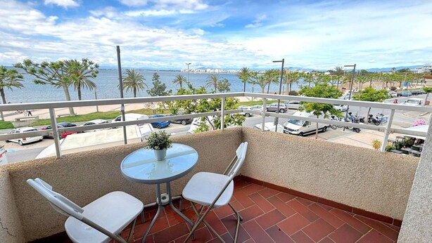 Un balcón con una mesa y sillas, con vista a una playa y un estacionamiento.